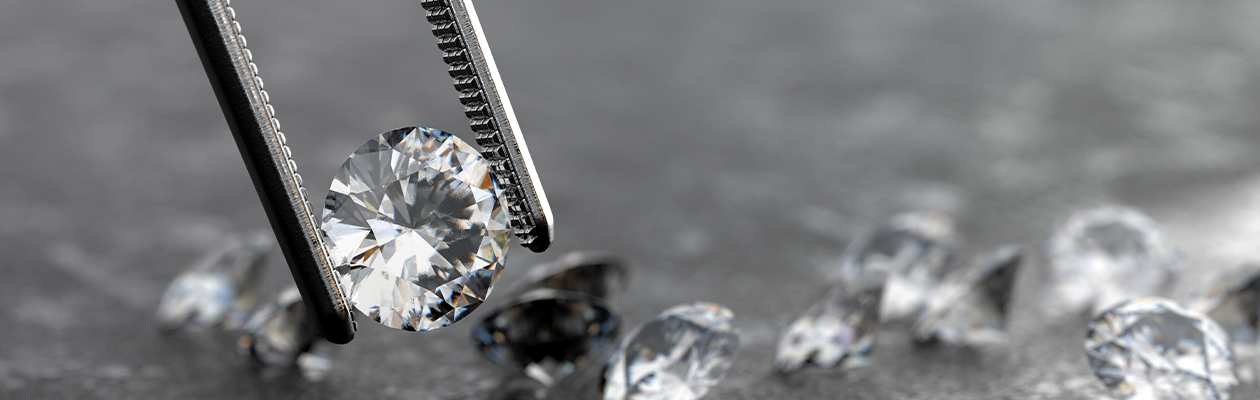 Diamond held by tweezers with other diamonds in the background on a dark surface